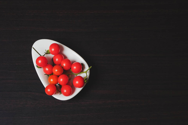 Small Tomato on black wood background.Food concept. - 写真・画像