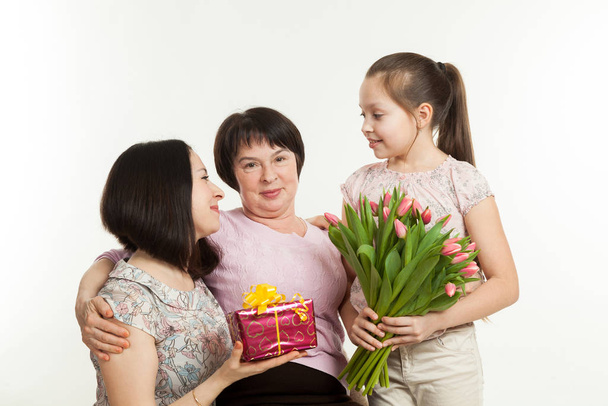 the daughter and the granddaughter give a bouquet of tulips to the grandmother - Foto, Bild