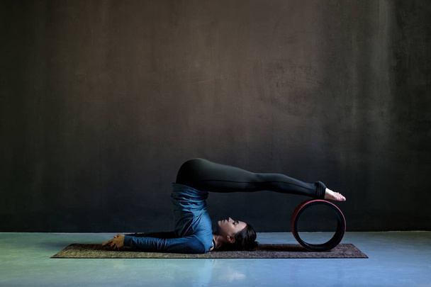 Girl in halasana pose doing yoga on black background. - Foto, Bild