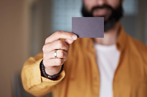 Bearded young man giving hand empty black business card on blurred background. Mockup Copy Paste Blank Advertisement. - Photo, image