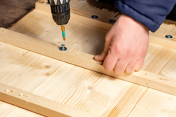 Male hands screw wooden blocks to the boards with a screwdriver - Фото, изображение