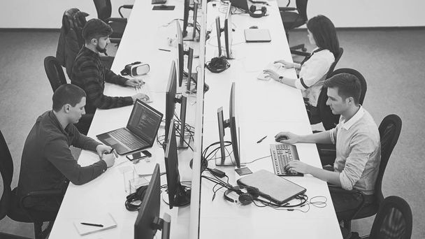 Jóvenes profesionales trabajando en una oficina moderna. Grupo de desarrolladores o programadores sentados en escritorios enfocados en computadoras en el espacio abierto de la compañía de TI. Equipo en el trabajo. Imagen de alta calidad
. - Foto, imagen