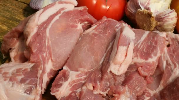 Steaky ze syrového masa jsou nakrájen z velkého kusu vepřového nebo hovězího masa na dřevěné řezací desce. Zelenina: rajčata, sladká paprika, česnek. Close-up. - Záběry, video