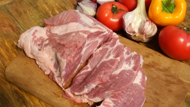 Çiğ et biftek ahşap bir kesme tahtası üzerinde domuz eti veya sığır eti büyük bir parça kesilir. Sebzeler: domates, tatlı biber, sarımsak. Close. - Video, Çekim