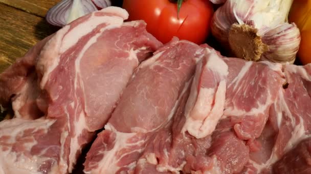 Os bifes de carne crua são cortados de um grande pedaço de porco ou carne bovina em uma tábua de corte de madeira. Legumes: tomates, pimentas doces, alho. Close-up
. - Filmagem, Vídeo