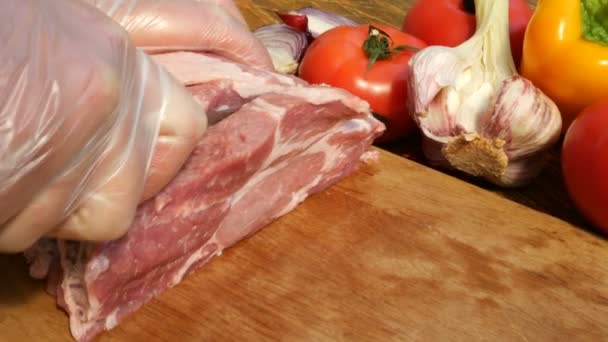 Rauwe vlees steaks zijn gesneden uit een groot stuk van varkensvlees of rundvlees op een houten snijplank. Groenten: tomaten, paprika, knoflook. Close-up. - Video