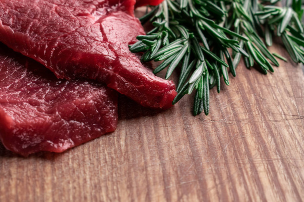 raw beef steak with fresh rosemary on a wooden board with space  - Photo, Image