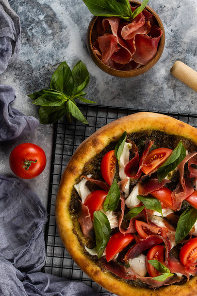 Pizza assada com presunto e legumes em mesa de mármore cinza com ingredientes
 - Foto, Imagem