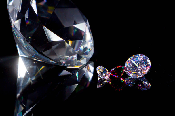 Diamant énorme et plusieurs cristaux chics sur une surface miroir noir profond, scintillement et éclat
 - Photo, image