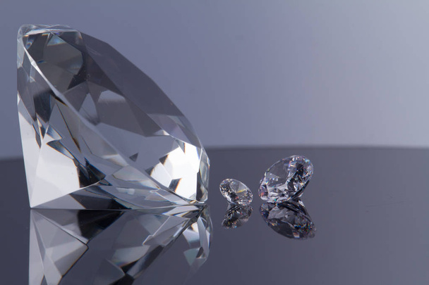 Величезний діамант і кілька шикарних кристалів на поверхні чорного дзеркала і білого фону, мерехтіння і іскри
 - Фото, зображення