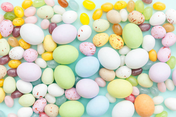 Happy Easter concept. Easter candy chocolate eggs and jellybean sweets isolated on trendy pastel blue background. Simple minimalism flat lay top view copy space - Фото, изображение