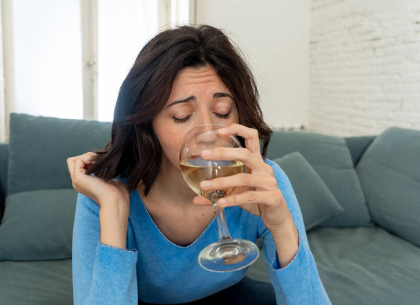 Portrait of depressed woman drinking glass of wine alone at home. Feeling distress, hopeless and frustrated, trying to feel better drinking. Unhealthy behavior, depression and alcohol concept. - Photo, Image