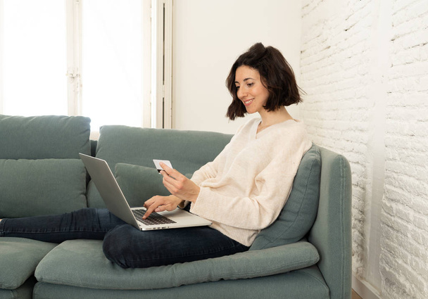 Happy young woman sitting with laptop and a credit card shopping online at home - Foto, Bild