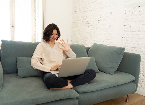 Happy young woman working on her laptop sitting cross-legged on the sofa. In technology concept - Fotografie, Obrázek