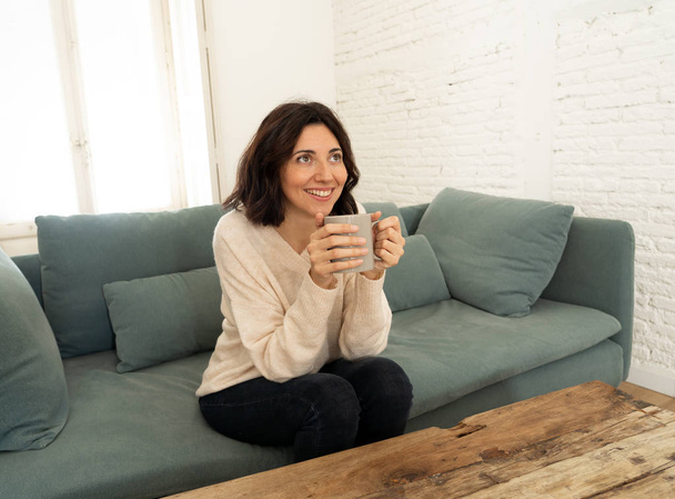 Lifestyle portrait of young pretty relaxed woman drinking hot coffee or chocolate feeling happy and cozy at home smiling happy on the couch. In leisure, peaceful life, happiness lifestyle concept. - Valokuva, kuva
