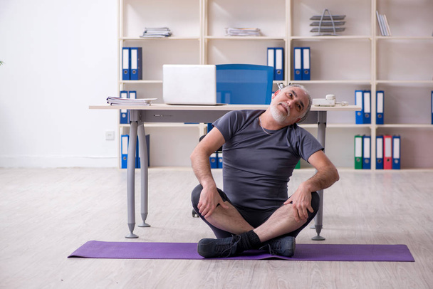 White bearded old man employee doing exercises in the office  - Foto, immagini