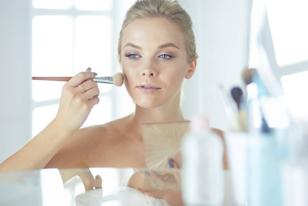 A picture of a young woman applying face powder in the bathroom - Photo, image