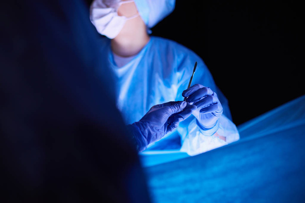 Doctor performing surgery in a dark background. - 写真・画像