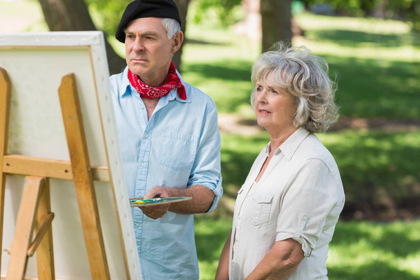 Woman watching mature man paint on canvas in the park - Foto, immagini