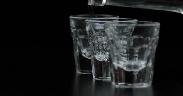 Derramar três doses de vodka de uma garrafa em vidro. Fundo preto
 - Filmagem, Vídeo