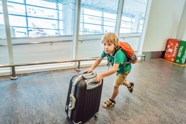 Funny little boy going on vacations trip with suitcase at airport, indoors - Zdjęcie, obraz