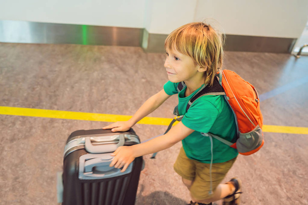 grappige kleine jongen gaan op vakantie reis met koffer op luchthaven, binnenshuis - Foto, afbeelding