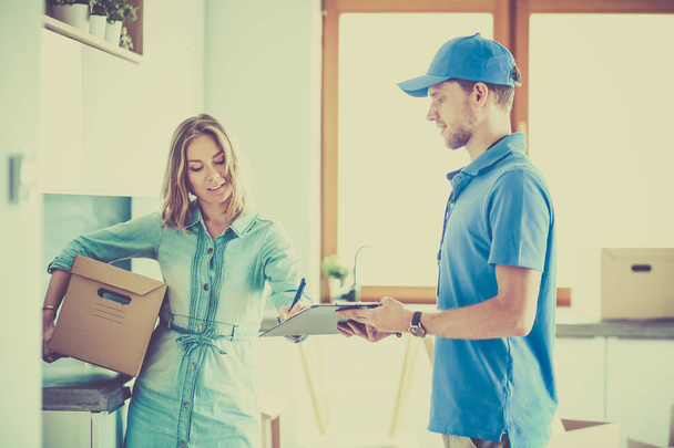 Smiling delivery man in blue uniform delivering parcel box to recipient - courier service concept - Foto, Bild