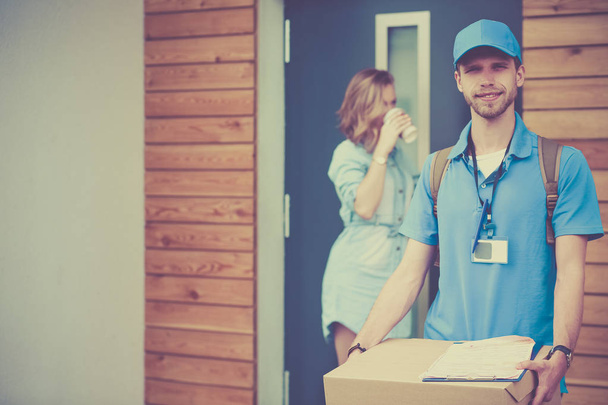 Smiling delivery man in blue uniform delivering parcel box to recipient - courier service concept - Foto, afbeelding