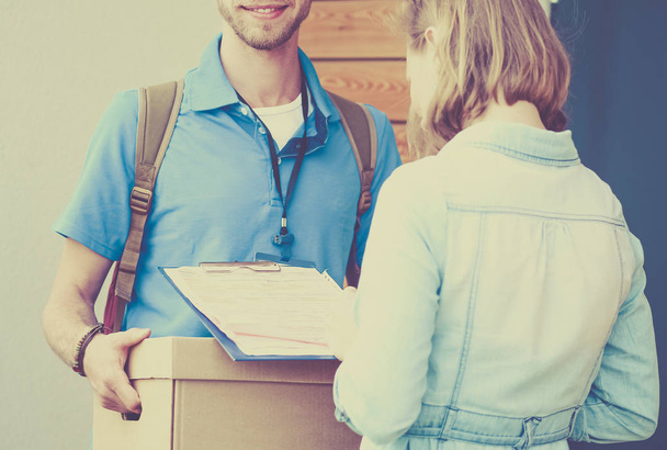 Homem de entrega sorridente em uniforme azul entregando caixa de encomendas ao destinatário - conceito de serviço de correio - Foto, Imagem