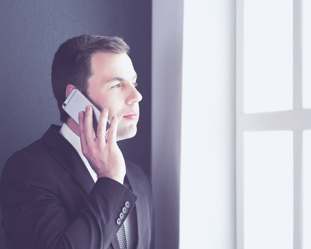 Handsome businessman talking on mobile phone in modern office. - Fotó, kép