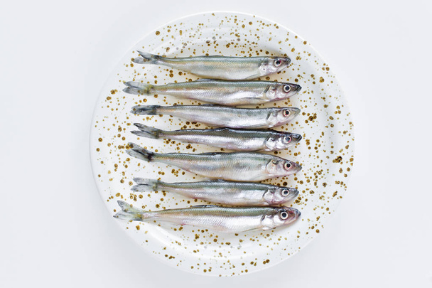 Raw smelt on a plate. White background, top view, space for text. - Фото, изображение