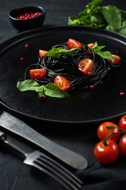 Вегетарианское блюдо, черные спагетти с базиликом и помидорами черри. Черный фон, вид сверху
. - Фото, изображение