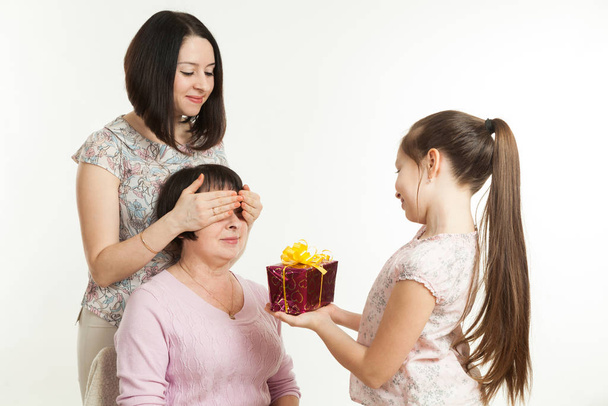 the daughter and the granddaughter give a gift to the grandmother - Foto, Imagen