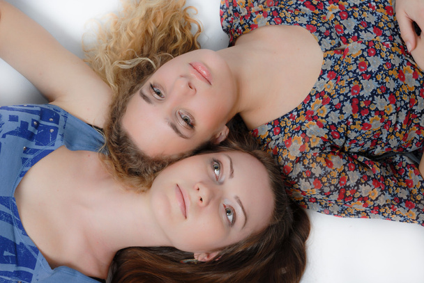 Дві красиві молоді дівчата лежать на голові і дивляться вгору на білому тлі
 - Фото, зображення