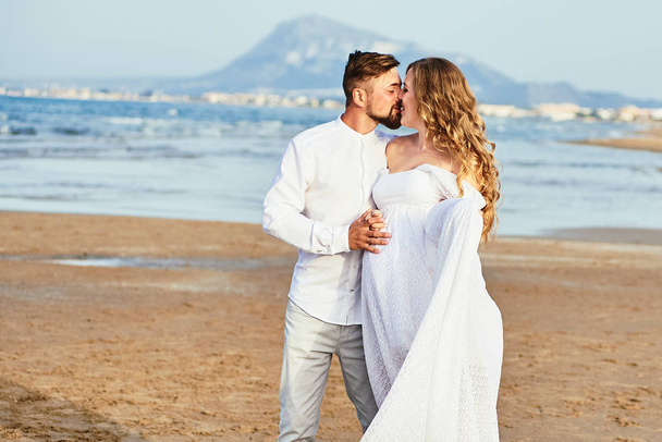 Young man kissing his beautiful pregnant wife in white dress - Photo, Image