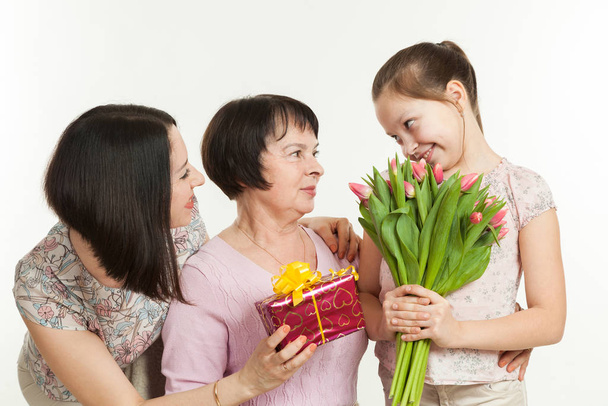 the daughter and the granddaughter give a bouquet of tulips to the grandmother - Foto, Bild