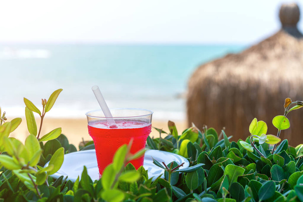 лето, стакан свежего сока, со льдом, из красных тропических фруктов на пляже, на зеленой траве, против моря
 - Фото, изображение
