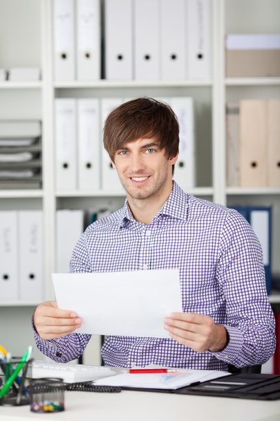 Young Businessman Holding Paper At Desk - Photo, image