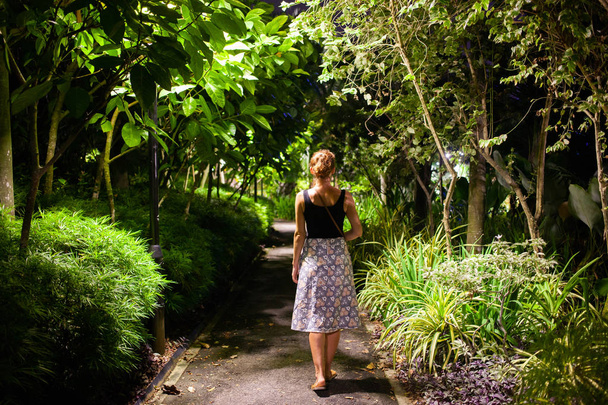mulher andando em um parque com árvores tropicais à noite
 - Foto, Imagem