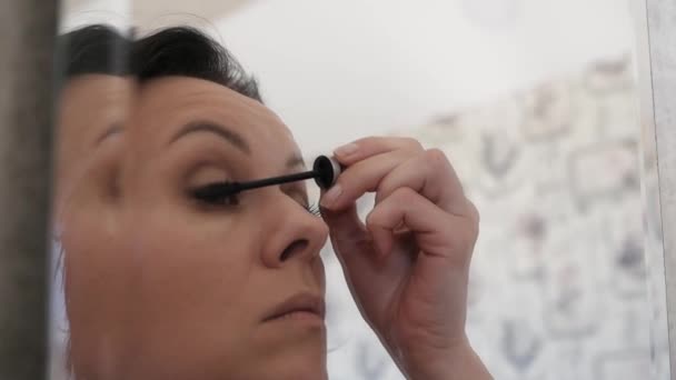 A nice woman paints her eyelashes in front of a mirror. - Video