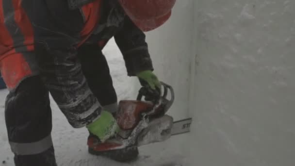 Worker cuts ice panel with gasoline saw Workman installer in an orange reflective vest and helmet customize chainsaw ice plate - Séquence, vidéo