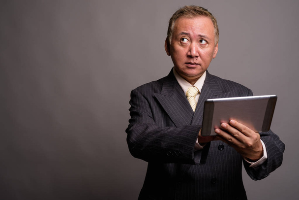 Portrait of mature Asian businessman against gray background - Photo, Image