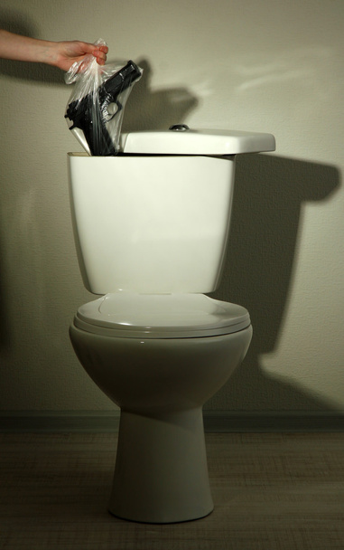 Hand hides gun in toilet tank in a bathroom - Фото, изображение