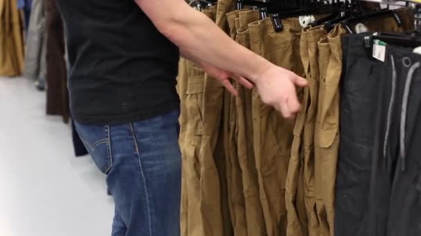 Mężczyzna w sklepie wybiera spodnie. Podnosi rozmiar. Koncepcja zakupów - Materiał filmowy, wideo