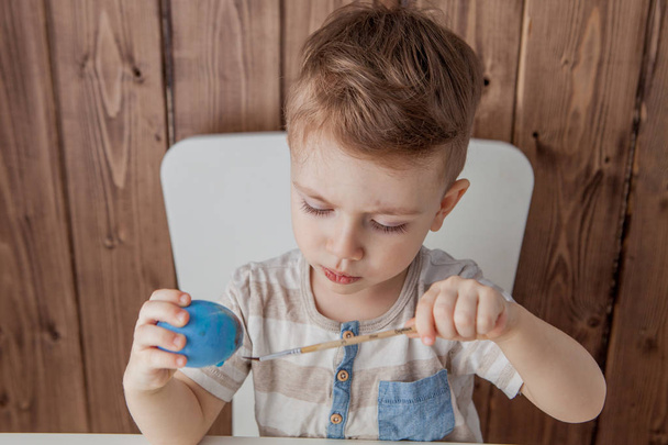 Little boy painting colorful eggs for easter on wooden backgroun - Fotografie, Obrázek