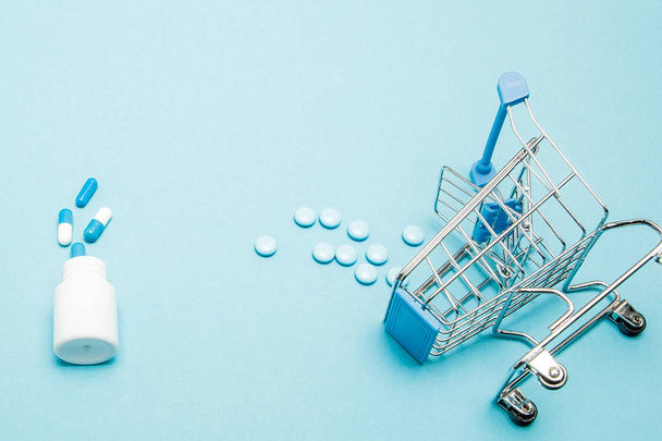 Pills and Shopping trolley on blue background. Creative idea for - Photo, Image