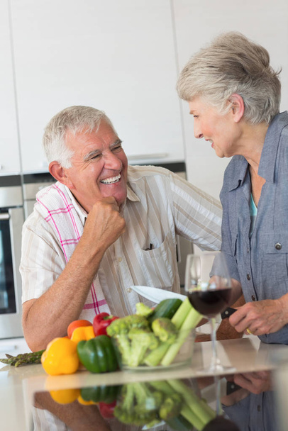 Smiling senior couple preparing a meal and having red wine at home in the kitchen - Foto, Bild