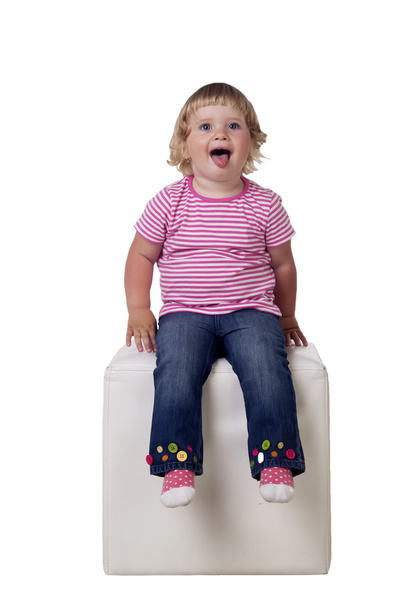 The little girl is sitting on a white cube, isolated on white background - Φωτογραφία, εικόνα