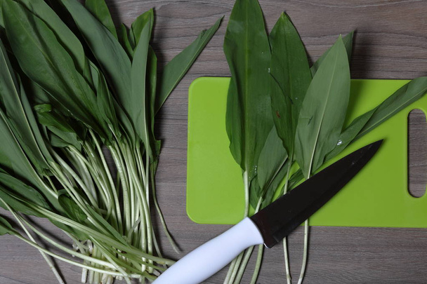 Fresh greens neatly laid out on the tabletop. Fragrant wild garlic. Next to the kitchen knife and cutting board. Ingredients for healthy salad. - Photo, image