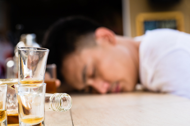 Пустые бутылки и стаканы перед пьяным человеком
 - Фото, изображение